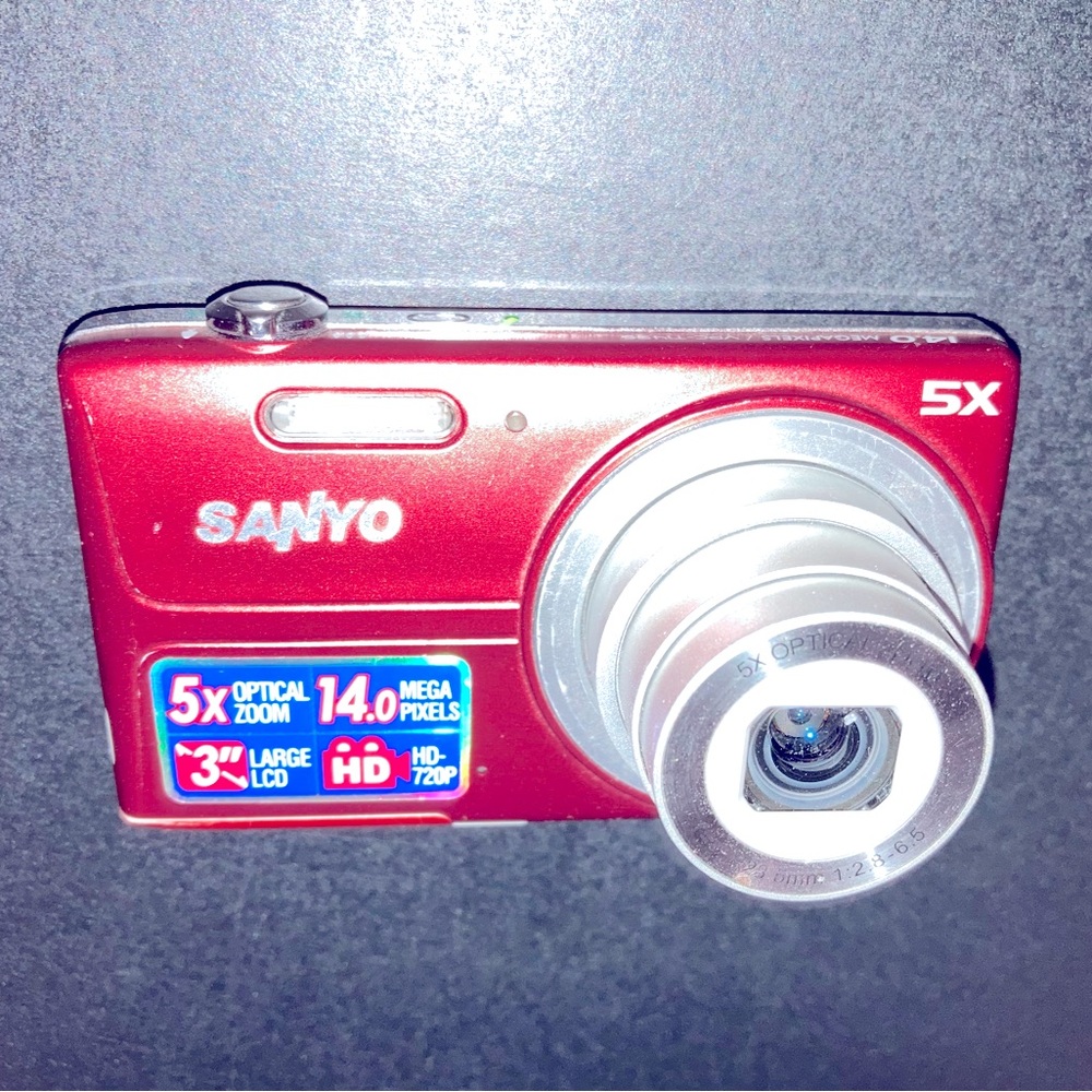 Red Sanyo digital camera. Charging cord comes with it and a 4 GB storage card.